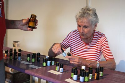 Anja Weigmann, die ehemalige Vorsitzende des Fördervereins, sitzt an einem Tisch. Auf dem Tisch stehen viele kleine Glasfläschchen mit Aromaölen. Sie hält zwei Fläschchen in Händen und betrachtet sie.