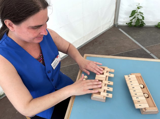 Eine Frau sitzt an einem Tisch und betastet ein haptisches Holzspielzeug, das aus nummerierten Klötzchen besteht.