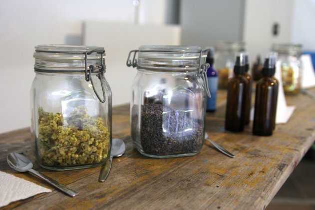 Verschiedene Glasbehälter mit getrockneten Kräutern und braune Glasflaschen auf einem Holztisch.